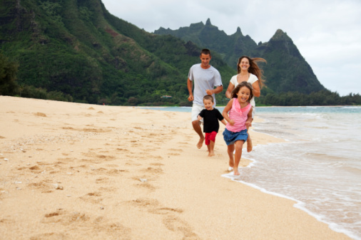 Full length view of a family running along shore in Kauai, HI; Tunnels Beach; some motion blur with focus on little boy; copy space 