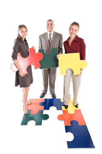 Three attracive business people hold large jigsaw puzzle pieces (puzzle made by photographer); copy space 
