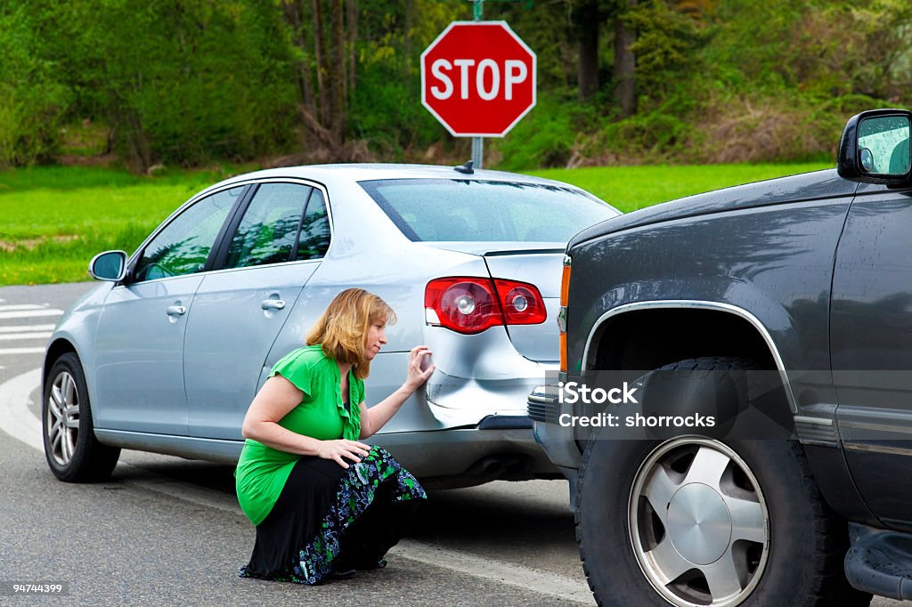 Woman Examining the Car Damage Full length photograph of an adult woman looking at her dented bumper with dissapointment; fender bender; copy space  Dented Stock Photo