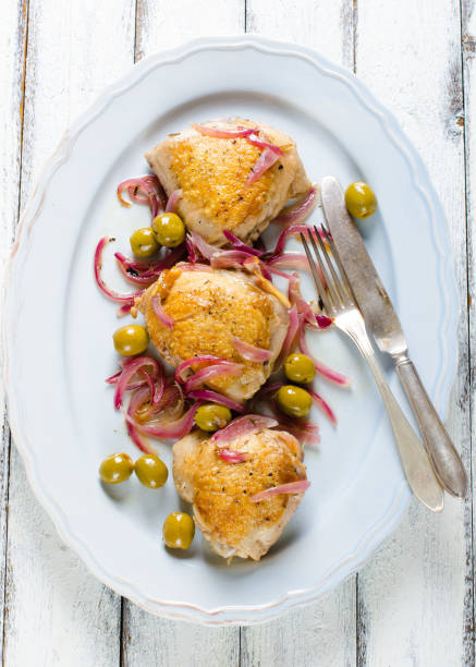 istock Roasted chicken thighs with olives and red onion on white wooden rustic background 947457736