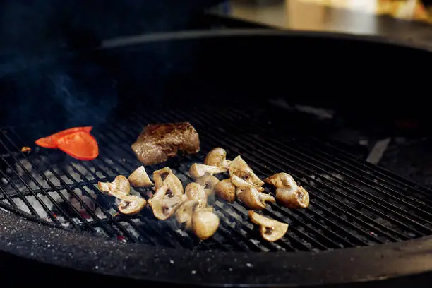 Photo of vegetables and meat grilling.  beefsteak mushrooms  tomatos garlic on grill. catering in food court at mall concept. space for text. modern kitchen. weekend picknick