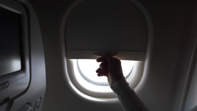 POV CLOSE UP: Woman opens the airplane window and lets blinding light into cabin