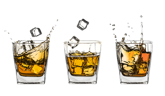 Three glasses of splashing whiskey with ice isolated on white