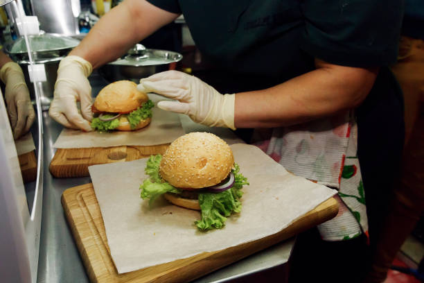 proceso de elaboración de hamburguesa. chef las manos en guantes de cocina hamburguesas y hamburguesas con queso, poner ingridients en escritorio de madera. catering en el patio de comidas en el concepto de centro comercial - dining burger outdoors restaurant fotografías e imágenes de stock