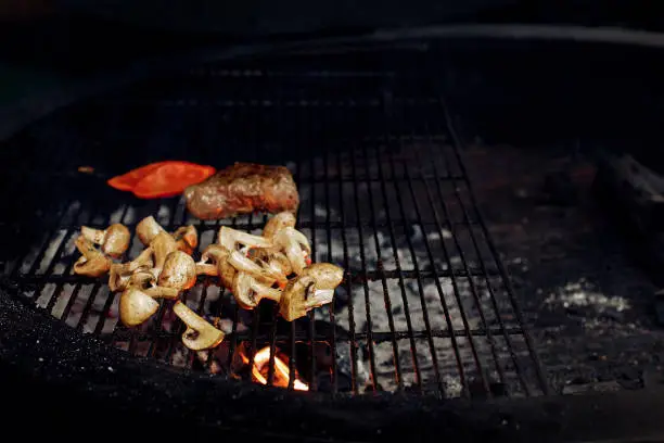 Photo of vegetables and meat grilling.  beefsteak mushrooms  tomatos garlic on grill. catering in food court at mall concept. space for text. modern kitchen. weekend picknick