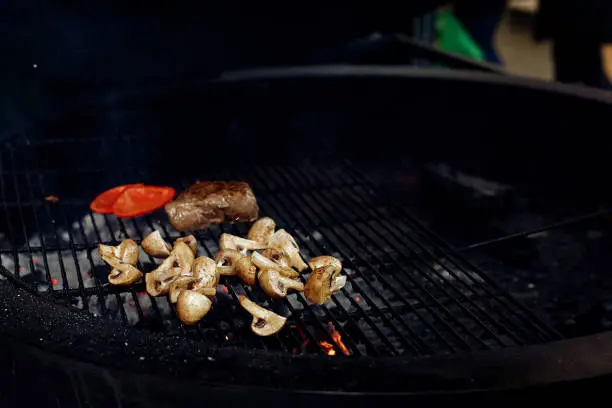 Photo of vegetables and meat grilling.  beefsteak mushrooms  tomatos garlic on grill. catering in food court at mall concept. space for text. modern kitchen.