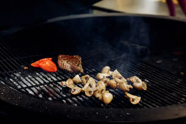 Photo of vegetables and meat grilling.  beefsteak mushrooms  tomatos garlic on grill. catering in food court at mall concept. space for text. modern kitchen. weekend picknick