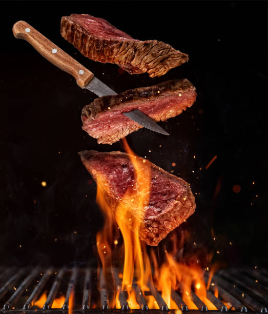 istock Flying pieces of beef steaks from grill grid on black background. 947471916