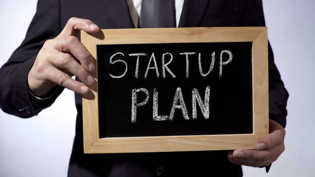 istock Startup plan written on blackboard, businessman holding sign, business concept 947472004