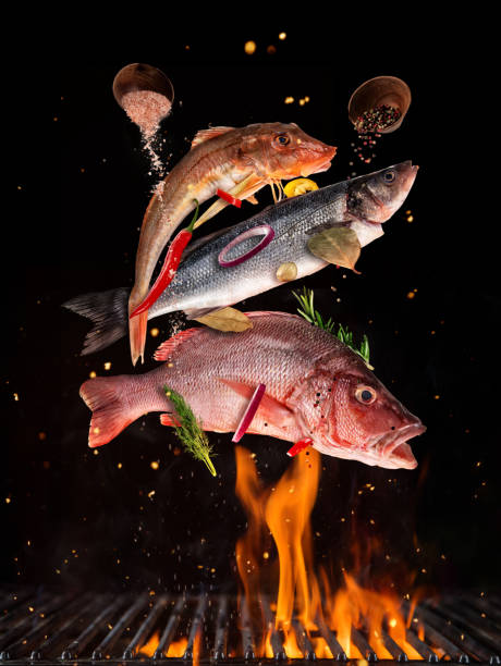 Flying raw whole fish from grill grid, isolated on black background