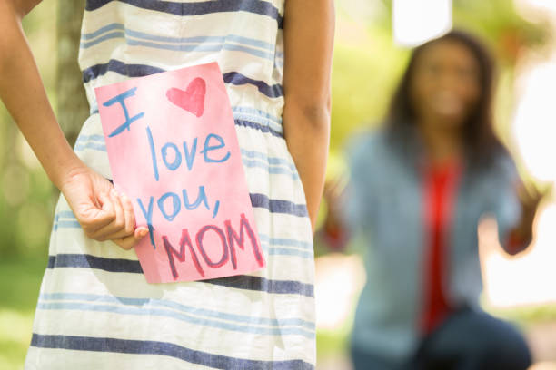 Happy Mother's Day. Little girl gives homemade card to her mom in front yard of family home. African descent family.