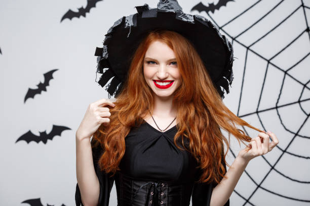 istock Halloween witch concept - Happy Halloween Witch holding posing over dark grey studio background with bat and spider web. 947483374