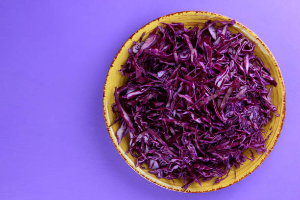Chopped cabbage on a violet background, red cabbage on a yellow plate, copy space, top view, vegetarian food, fresh vegetables for salad, ultraviolet background, minimalism