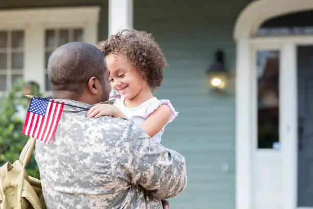 Young mixed race girl smiles while hugging her army dad. Her dad is home on leave.