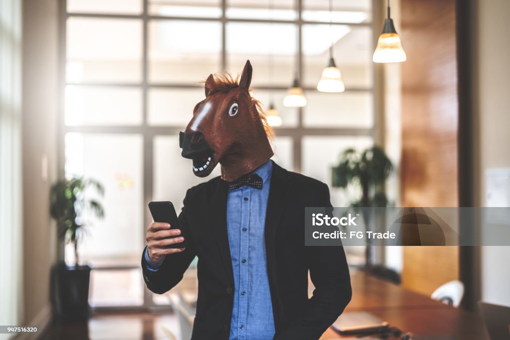 Business man with Horse Mask Using Mobile at Office Bizarre Businessman Stock Photo