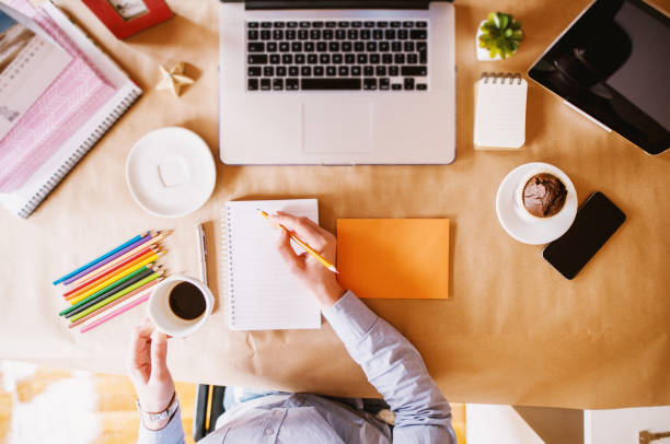 istock Top view of woman designer writing organization plans in notes while having a coffee break at the office desk. 947540512