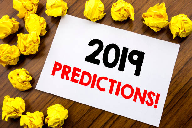 istock Handwritten text showing word 2019 Predictions. Business concept writing Forecast Predictive Written on sticky note paper, wooden background with space office view with folded yellow paper 947541216