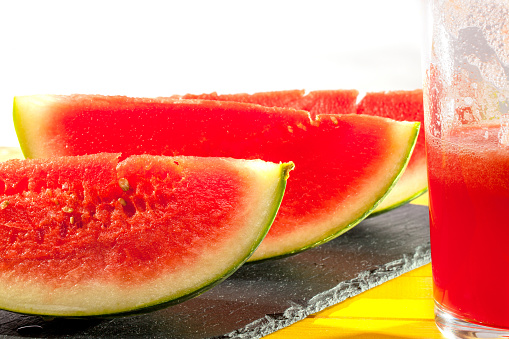 Freshly made vegan watermelon drink. Thirst quenching summer crush with fruit slices and half drunk glass of juice. Close up against white background.