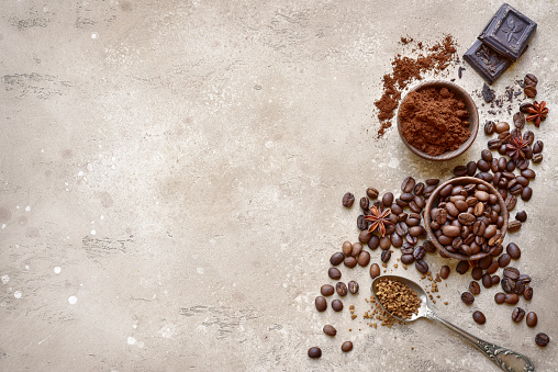 Ground coffee and coffee beans with spices over beige rustic slate, stone or concrete background.Top view with copy space.