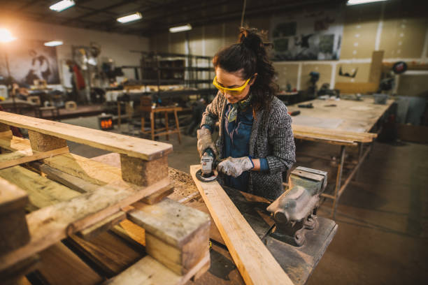 istock Portrait view of hardworking middle aged professional female carpenter worker working with sandpaper and choosing wood in the workshop. 947604716