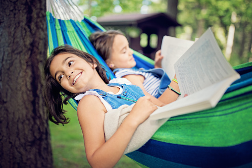 Two girls are lying down in the hammock and reading books