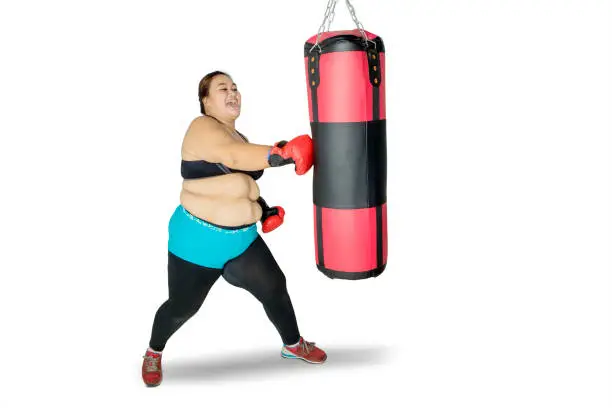 Picture of obese woman doing a workout while hitting a boxing bag, isolated on white background