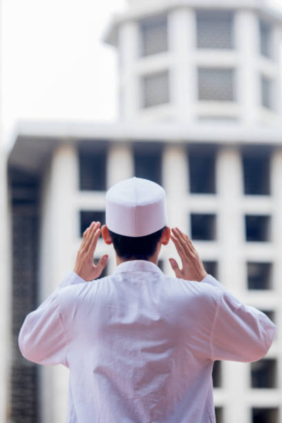 Young Muslim man doing azan in the mosque Rear view of a young Muslim man doing azan while standing in the mosque azan stock pictures, royalty-free photos & images