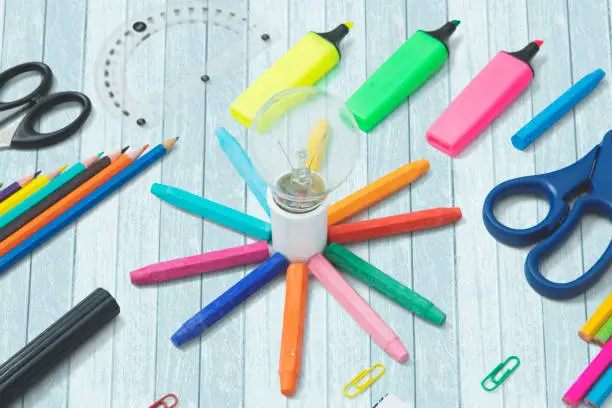 Closeup of a light bulb with colored crayons and school supplies on the table