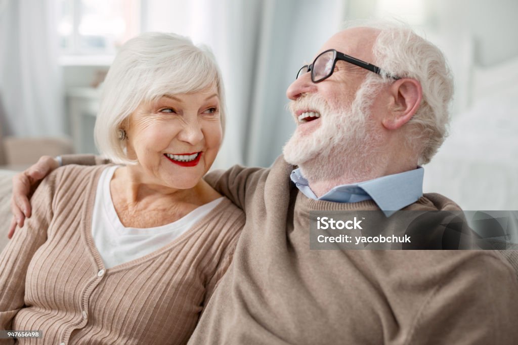 Cheerful elderly man hugging his wife Elderly couple. Cheerful elderly man sitting together with his wife while hugging her Lifestyles Stock Photo