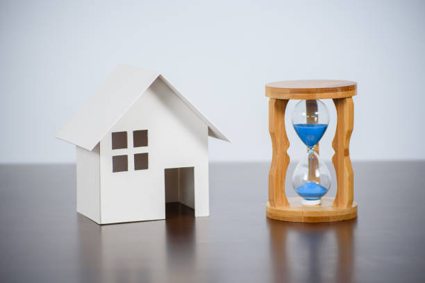 Hourglasses with model house on a wooden table. stock photo