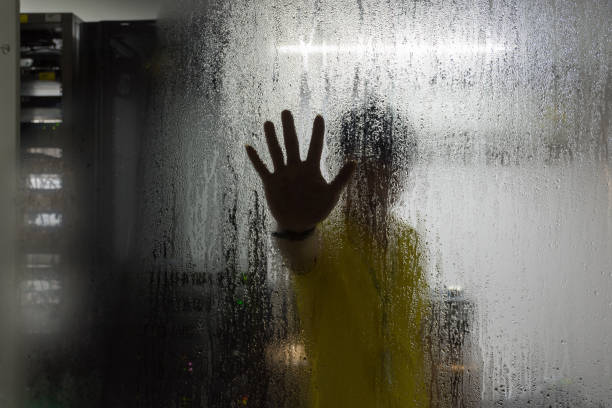 istock Silhouette of hand of man on glass with water drop in computer server mainframe room in data center 947714286