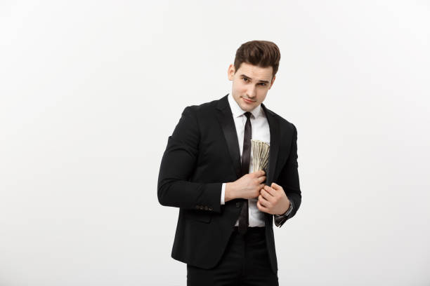 istock Business Concept: Handsome businessman in black suit taking dollars banknotes with stealthy expression against white background. 947721026