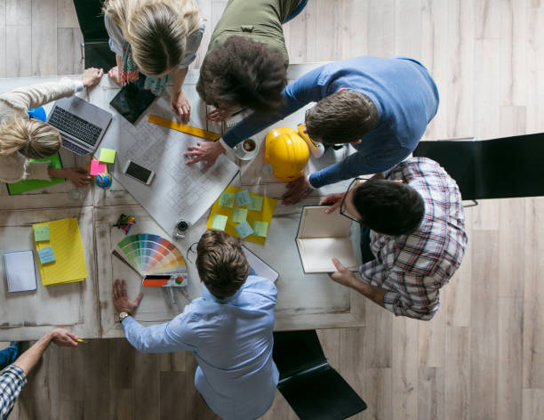 istock Above view of large group of architects cooperating while examining blueprints on a meeting in the office. 947725876