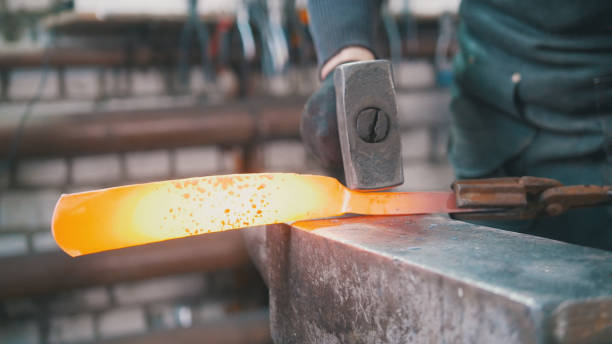 istock Muscular man blacksmith with hammer in forge creating steel knife 947726340