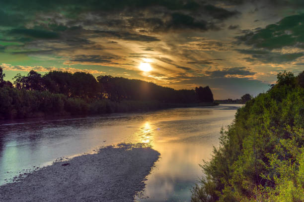 Sunset across the Manawatu river with dramatic skies with the sun and clouds reflecting on the river