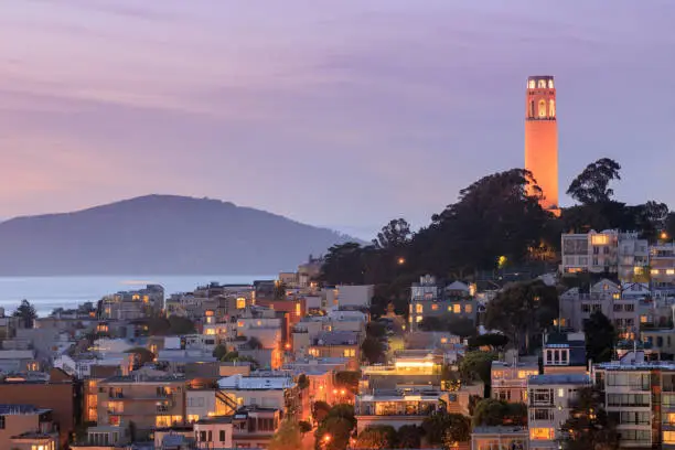Photo of Coit Tower on Telegraph Hill with San Francisco Bay and Angel Island in the background at dusk.