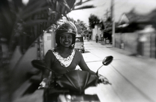 Negombo, Sri Lanka, December 13, 2015: A beautiful girl sits on a motor scooter and smiles. Attention! The image contains granularity and other artifacts of analog photography!