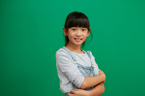 Studio portrait of confident little girl standing with her arms folded against a green background