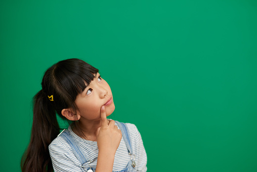 Full length view of beautiful little cheerful carefree girl in denim overalls having fun jumping barefoot on pink background.