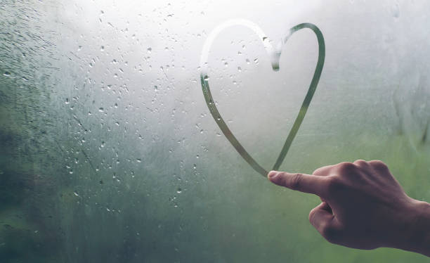 A man's hand is writing a heart-shaped glass window during a rain. stock photo