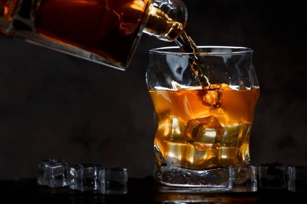 istock Whiskey bottle flowing into a glass of ice on a dark background 947768408