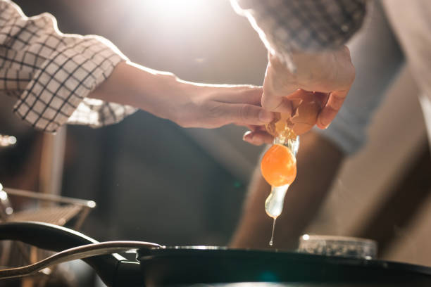 primo piano di una donna irriconoscibile che rompe un uovo prima di prepararlo in una padella. - break eggs domestic kitchen breaking foto e immagini stock