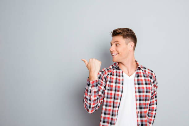 istock Young cheerful man showing direction on gray background 947780888