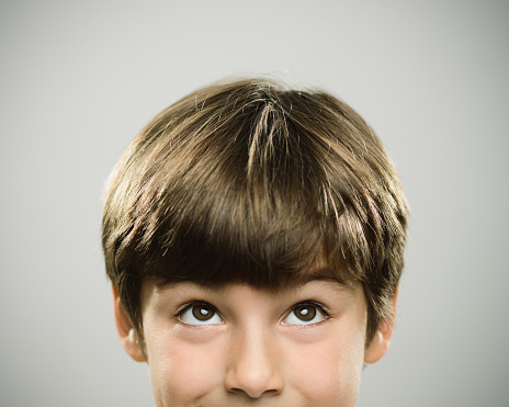 Close up half face portrait of a happy caucasian real kid looking up. The boy is 7 years old and has brown hair. Horizontal shot of little boy looking around against white background. Photography from a DSLR camera. Sharp focus on eyes.