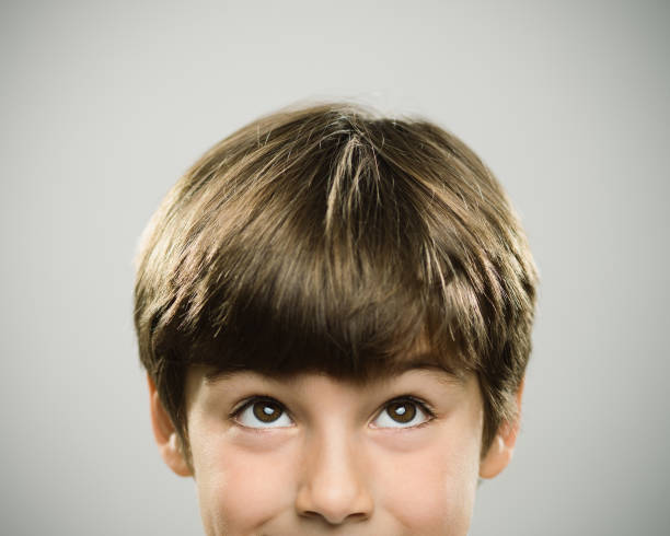 Portrait of a caucasian real boy looking up. Close up half face portrait of a happy caucasian real kid looking up. The boy is 7 years old and has brown hair. Horizontal shot of little boy looking around against white background. Photography from a DSLR camera. Sharp focus on eyes. looking around stock pictures, royalty-free photos & images