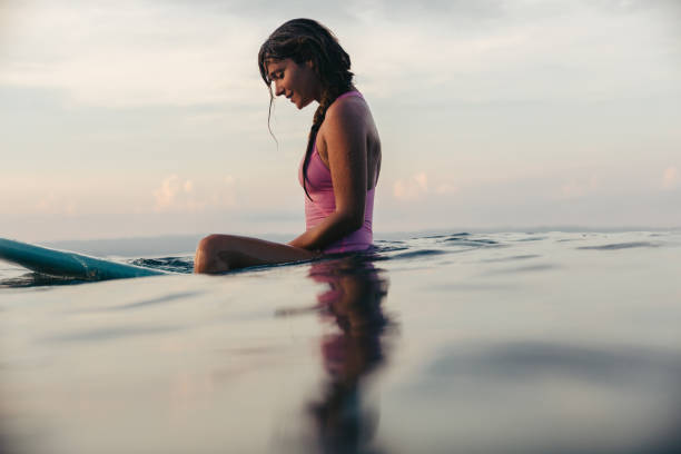 istock Sportswoman sitting on surfboard in water at sunset 947800280