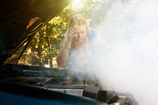 Young woman shocked by smoke or steam pouring from her car engine.