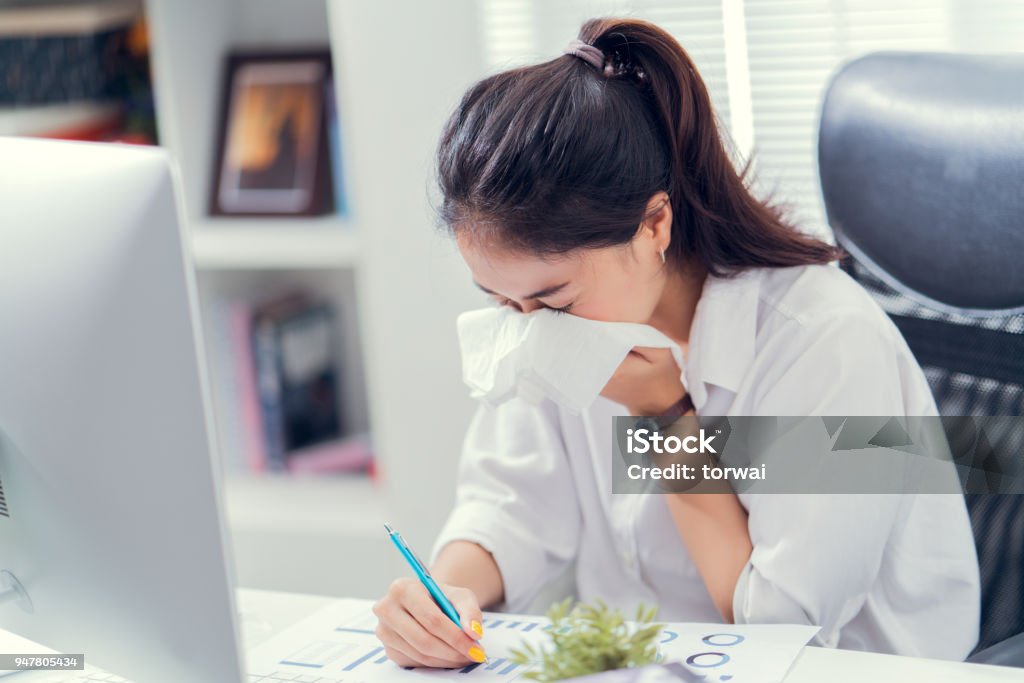 Women are sneezing and are cold. She is in the office. Office Stock Photo