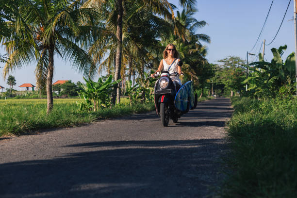istock young woman riding scooter with surfing board 947816634