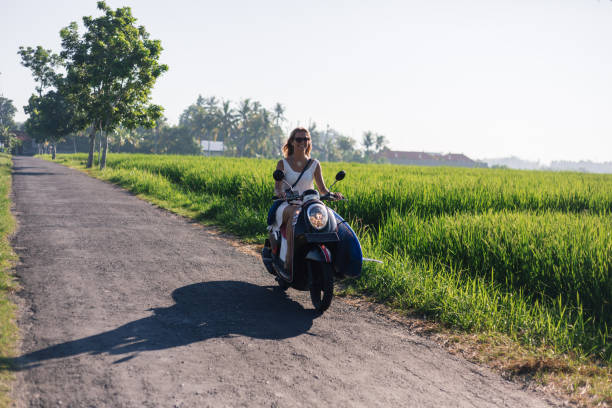 istock young woman riding scooter with surfing board on road 947819294